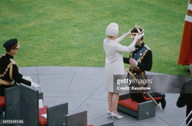 British Royal Prince Philip, Duke of Edinburgh watches as his wife, Elizabeth II, places the gold coronet onto the head of their son, Charles, Prince...