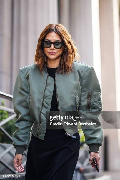 Christine Centenera wears black sunglasses, a black long midi dress, a khaki nylon zipper bomber coat, outside The Row, during Paris Fashion Week -...