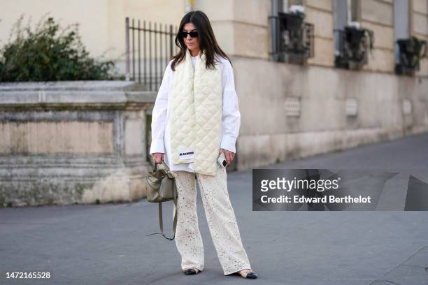 Guest wears black sunglasses, a white shirt, a pale yellow quilted puffy large scarf from Jil Sander, a khaki matte leather Puzzle handbag from...