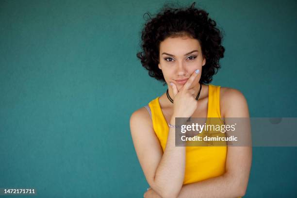 portrait of attractive young woman against green background - girl standing crossed arms studio stock pictures, royalty-free photos & images