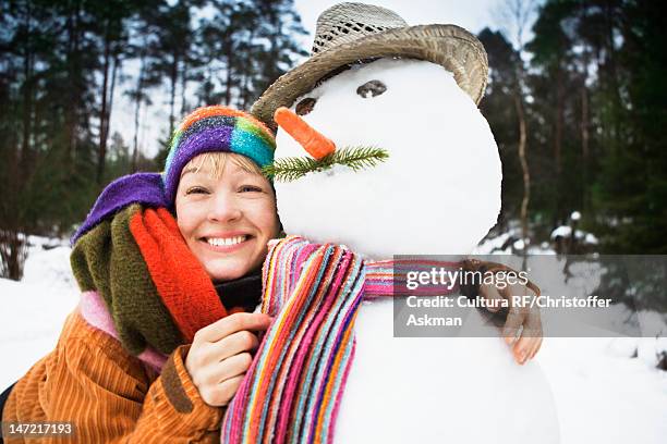 smiling woman hugging snowman - frau schneemann stock-fotos und bilder