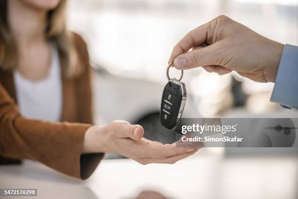 close-up car salesman giving the keys of a new car to his female customer,both sitting indoors at a office desk at a car dealer - car keys stock pictures, royalty-free photos & images