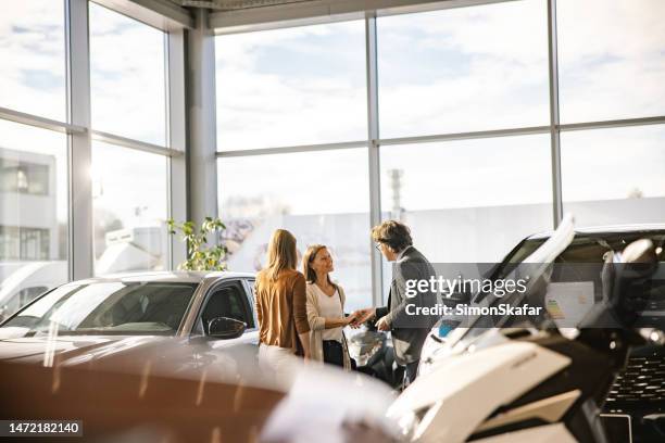 el hombre de negocios está dando las llaves a una clienta, ambos sonriendo el uno al otro, mujer con parada en el frente, en el interior de un concesionario de automóviles por la noche - salón de coches fotografías e imágenes de stock