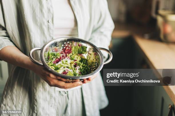 a mixture of green salad, arugula and spinach in the hands of a woman, washed in a colander - rucola stock-fotos und bilder