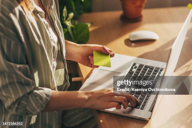 hands holding plastic credit card and using laptop. online shopping concept. toned picture - ama-de-casa-comprando fotografías e imágenes de stock