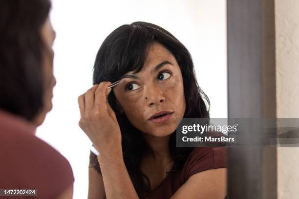 woman tweezing eyebrows in front of mirror - tweezing eyebrows stock pictures, royalty-free photos & images