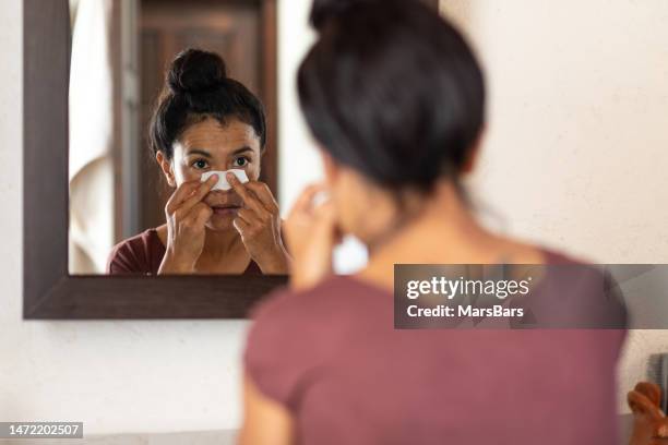 woman applying pore strips on nose in bathroom - pores stockfoto's en -beelden