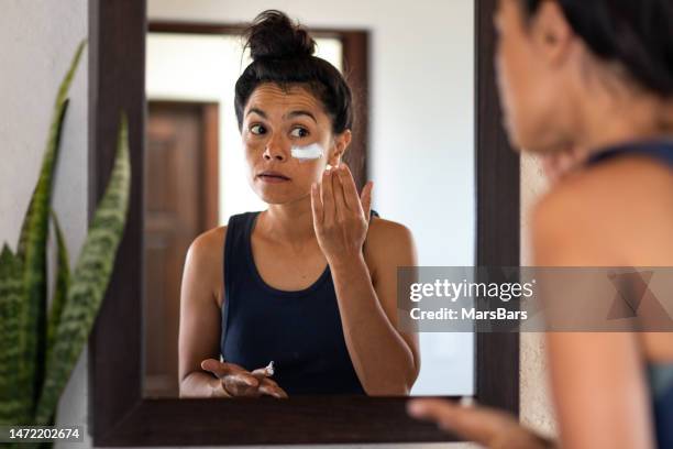 woman applying white sunblock to face, looking at
 bathroom mirror - suncream stock pictures, royalty-free photos & images