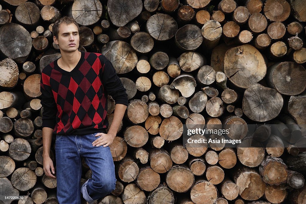 Young man leaning against wall of stacked logs
