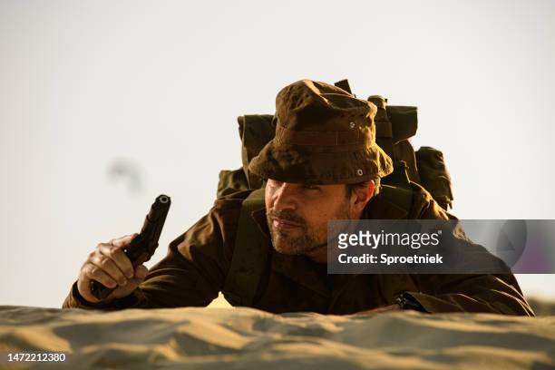 bearded soldier with pistol lying prone on dune - concentration camp stock pictures, royalty-free photos & images