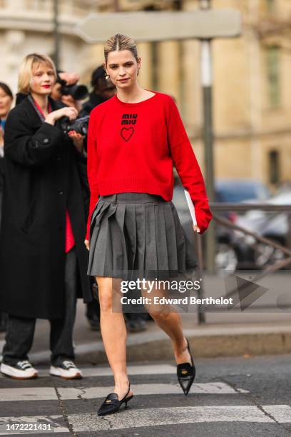 Guest wears gold earrings , a neon red with black logo pullover from Miu Miu, a dark gray pleated / accordion short skirt form Miu Miu, a black faded...