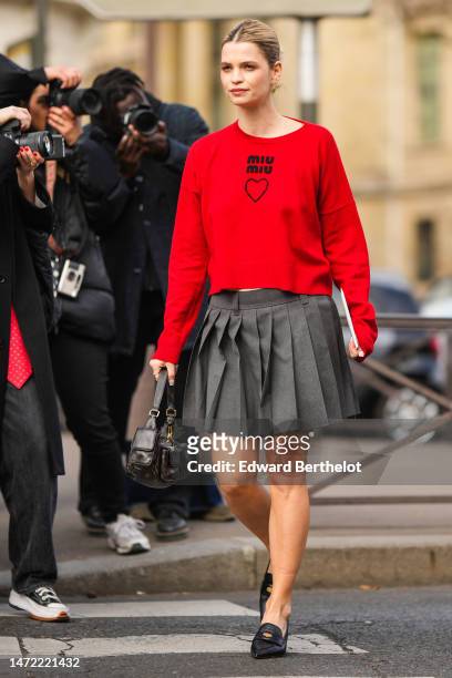 Guest wears gold earrings , a neon red with black logo pullover from Miu Miu, a dark gray pleated / accordion short skirt form Miu Miu, a black faded...