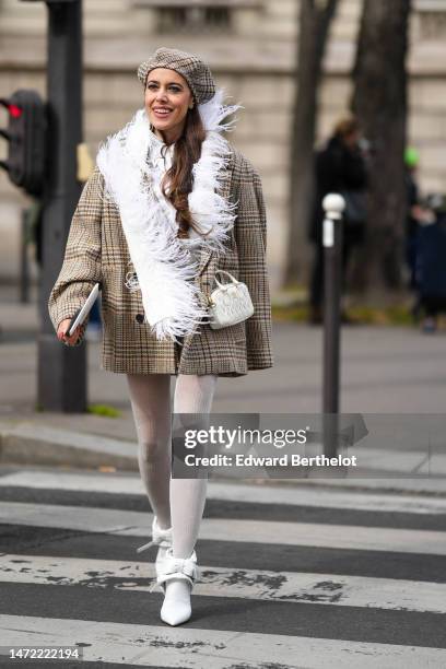 Guest wears a beige with embroidered brown and blue print pattern wool beret, diamonds earrings, a white shirt, a white feathers boa scarf, a beige...