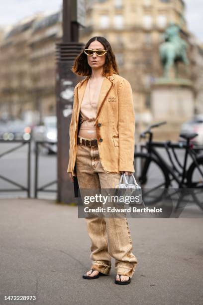 Guest wears beige gold sunglasses, a beige buttoned / V-neck cropped gilet from Miu Miu, a brown orange faded denim blazer jacket from Miu Miu, a...