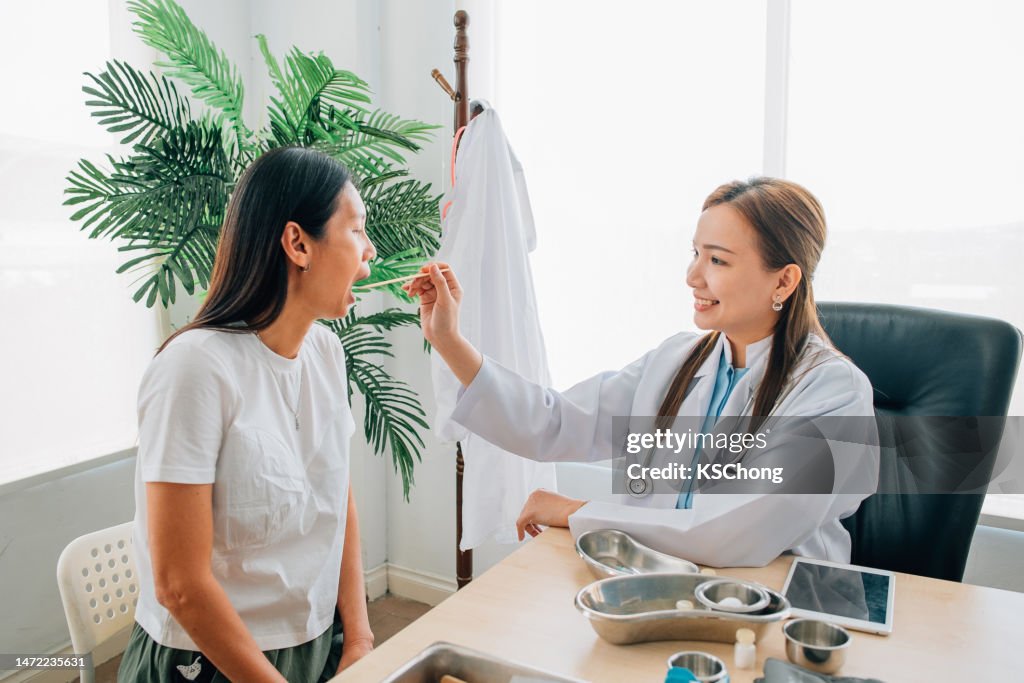 Asian Chinese doctor checking her patient throat in her office