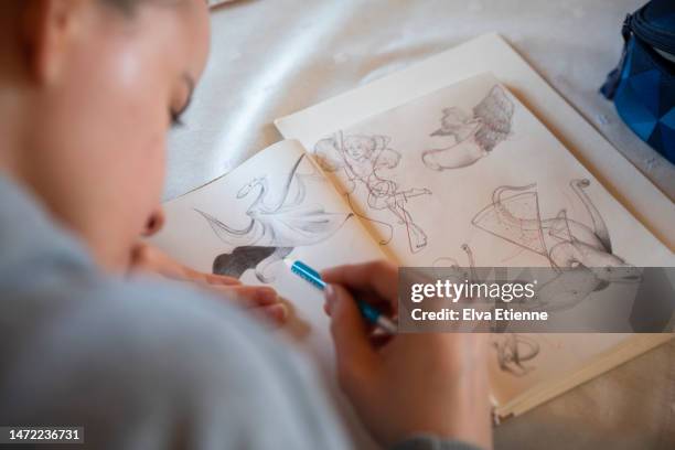 teenager sitting at a dining table, sketching with a pencil in a notebook. - draw stock pictures, royalty-free photos & images