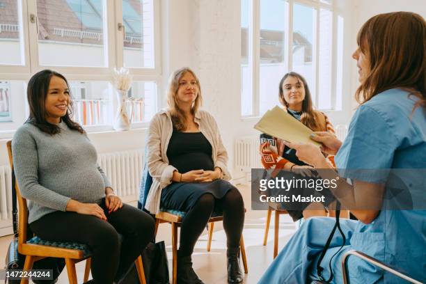 side view of female doctor discussing with pregnant women during antenatal class at clinic - prenatal class stock pictures, royalty-free photos & images
