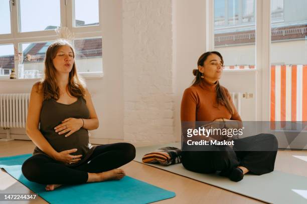 expectant women practicing breathing exercise sitting cross-legged on exercise mat in yoga class - atemübung yoga 30 bis 40 jahre stock-fotos und bilder