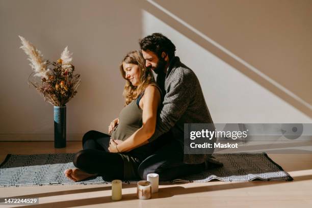 expectant couple doing yoga sitting on rug against wall in exercise room - pregnant yoga stock-fotos und bilder