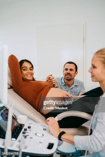 smiling pregnant woman with man doing ultrasound at maternity clinic - prenatal care stockfoto's en -beelden