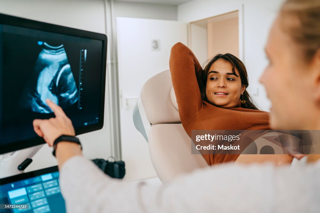 Pregnant woman looking at computer screen with ultrasound image shown by doctor at clinic