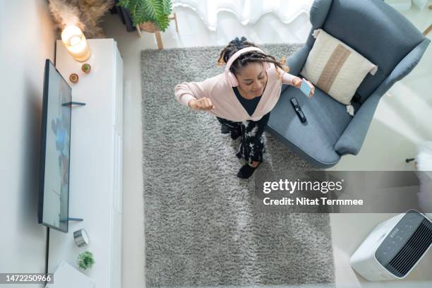 music can help to reduce symptoms of depression. high angle view of african american young woman dancing and listening to music with a smartphone in the living room at home. - smart tv living room stock pictures, royalty-free photos & images