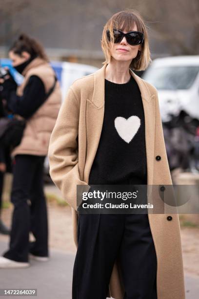 Anya Ziourova wears a black sweater with white heart print, black trousers and beige coat, outside Chanel, during Paris Fashion Week - Womenswear...