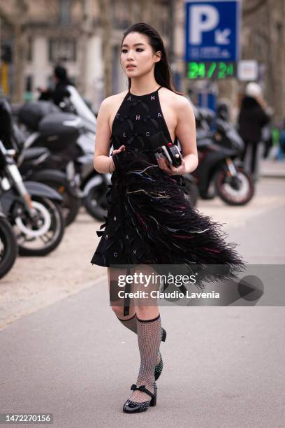 Guest wears a decorated Chanel black mini dress, decorated Chanel heels, outside Chanel, during Paris Fashion Week - Womenswear Fall Winter 2023...