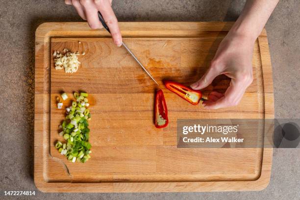 a person chopping red chilli pepper on wooden chopping board. - chopped stock pictures, royalty-free photos & images