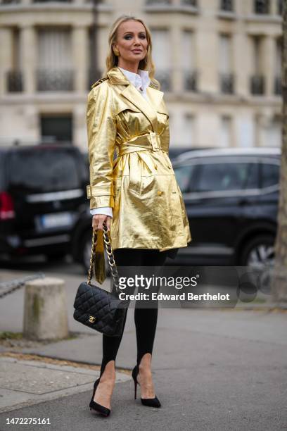 Guest wears gold large earrings, a white shirt, a gold shiny leather belted / buttoned coat, black fuseau legging pants, black shiny leather handbag...