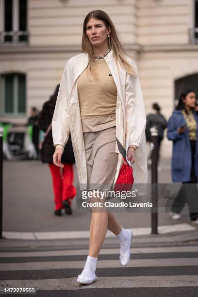 Veronika Heilbrunner wears a beige Miu Miu t-shirt, cream jacket, beige skirt and red Miu Miu bag, outside Miu Miu, during Paris Fashion Week -...