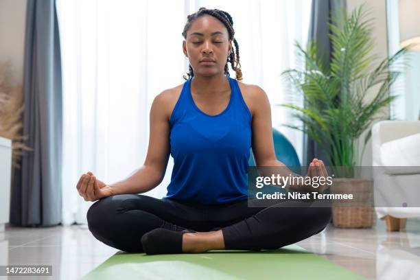 regulate your mood and enhance physical performance with yoga meditation. african american females doing yoga meditation to improve sleep quality and maintain heart health in the living room at her home. - yoga pose stock-fotos und bilder