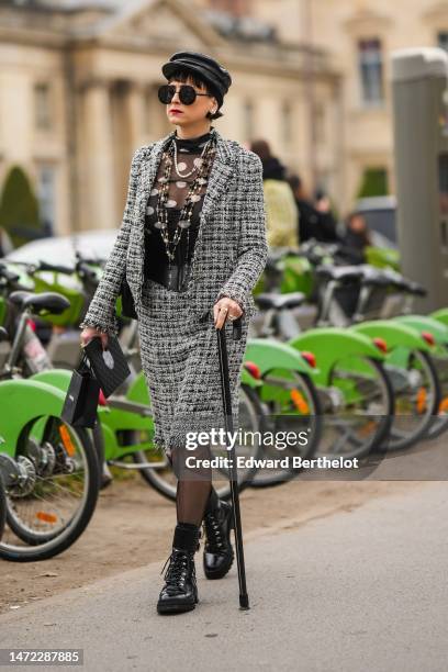 Guest wears a black shiny leather crocodile print pattern cap, black circle sunglasses, diamonds earrings, a black tulle with white polka dots print...