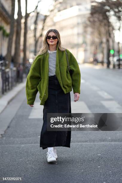 Guest wears black sunglasses, a white and black striped print pattern t-shirt, a green fluffy oversized jacket, a black long denim skirt, white...