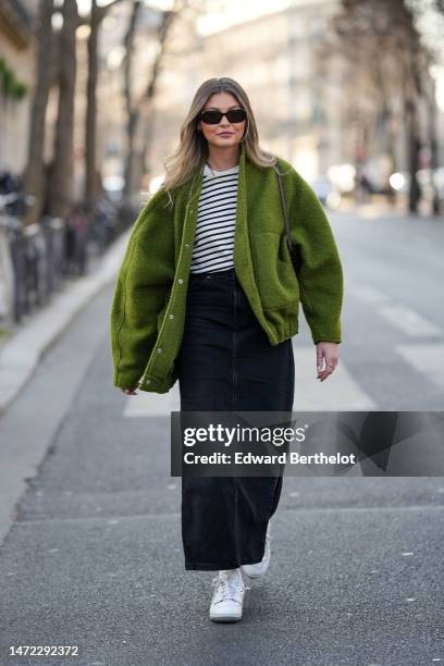 Guest wears black sunglasses, a white and black striped print pattern t-shirt, a green fluffy oversized jacket, a black long denim skirt, white...