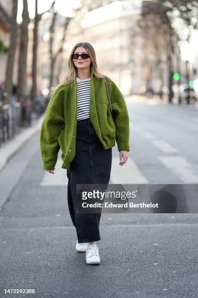 Guest wears black sunglasses, a white and black striped print pattern t-shirt, a green fluffy oversized jacket, a black long denim skirt, white...