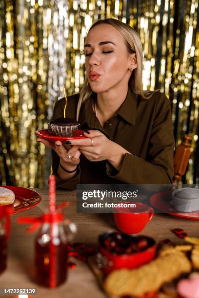 fröhliche junge frau bläst die geburtstagskerze auf einem schokoladenmuffin aus - chocolate foil stock-fotos und bilder