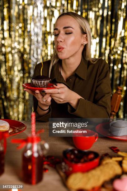 cheerful young woman blowing out the birthday candle on a chocolate muffin - chocolate foil stock pictures, royalty-free photos & images