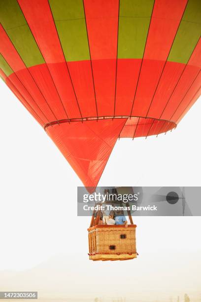 wide shot of couple taking selfie during sunrise hot air balloon ride - hot air balloon ride stock-fotos und bilder