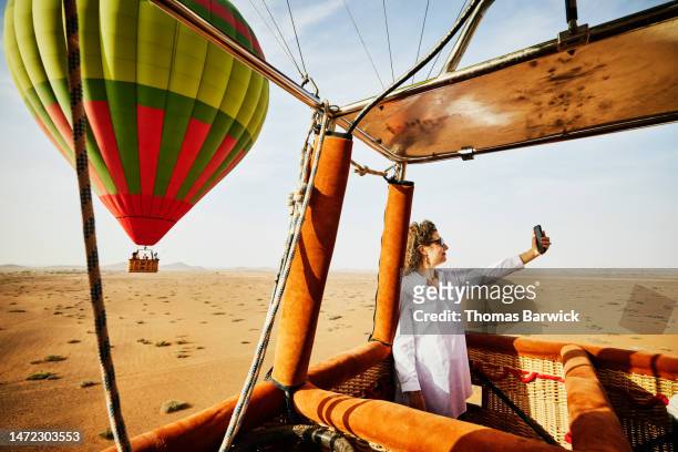 wide shot woman taking selfie during sunrise hot air balloon ride - hot air balloon ride stock-fotos und bilder