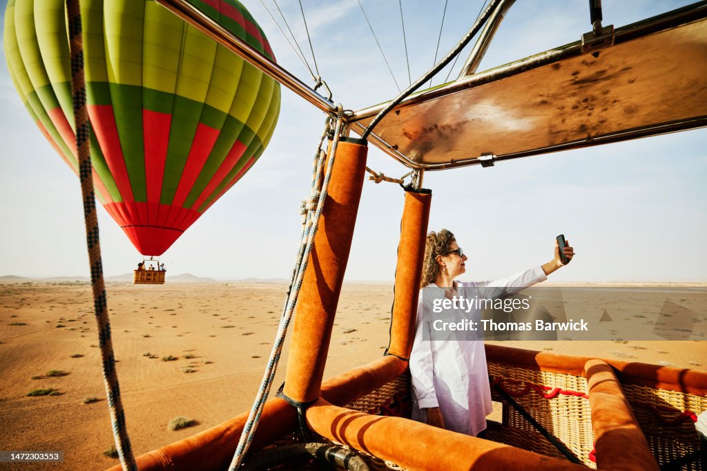 Wide shot woman taking selfie during sunrise hot air balloon ride