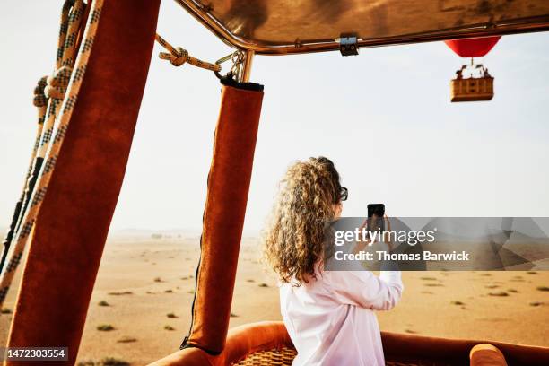 medium shot woman taking photos during sunrise hot air balloon ride - toma mediana fotografías e imágenes de stock