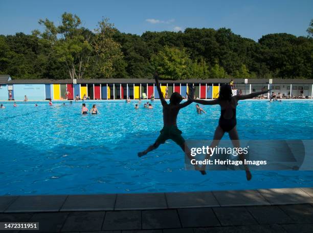 Tooting Bec Lido, Tooting Bec Road, Streatham, Wandsworth, Greater London Authority, 2013. Two children, silhouetted against the water, jumping into...