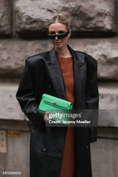 Leonie Hanne wears green Hermes bag, rust brown dress, black long leather coat and black sunglasses, outside Hermes during Paris Fashion Week -...