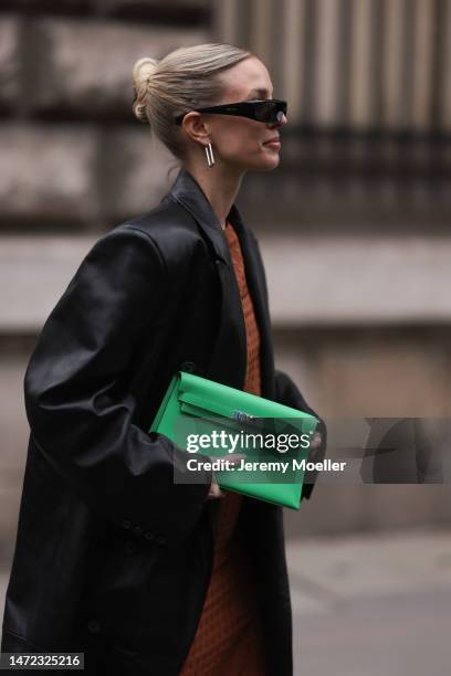 Leonie Hanne wears green Hermes bag, rust brown dress, black long leather coat and black sunglasses, outside Hermes during Paris Fashion Week -...