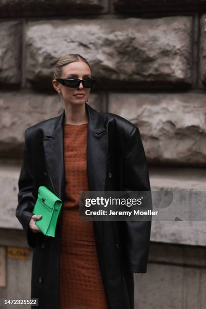 Leonie Hanne wears green Hermes bag, rust brown dress, black long leather coat and black sunglasses, outside Hermes during Paris Fashion Week -...