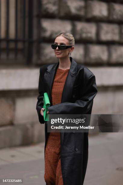 Leonie Hanne wears green Hermes bag, rust brown dress, black long leather coat and black sunglasses, outside Hermes during Paris Fashion Week -...