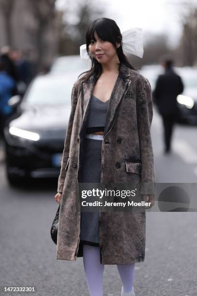 Susie Lau seen wearing a dark grey coat, a grey cropped top and matching grey skirt, a white hair bow, white tights and white shoes and a black bag...