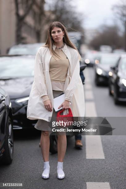 Veronika Heilbrunner seen wearing a white long coat, a beige shirt and a grey skirt, white ballet flats, white socks and a red bag before the Miu Miu...