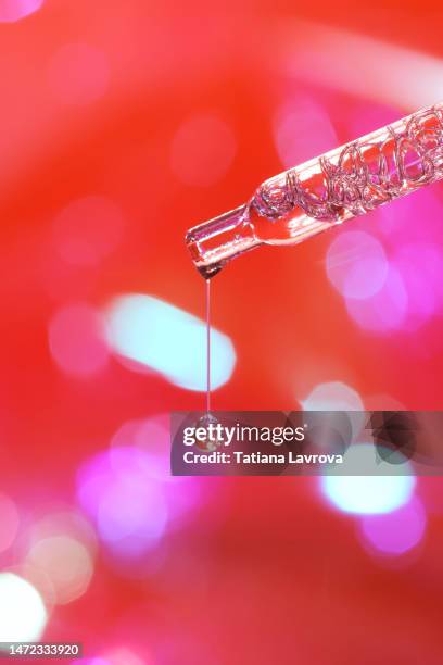 drop of face serum falling from glass pipette on purple red blurred background. beauty, cosmetic products, wellness, skin and body care concept - clear skin red background stock-fotos und bilder